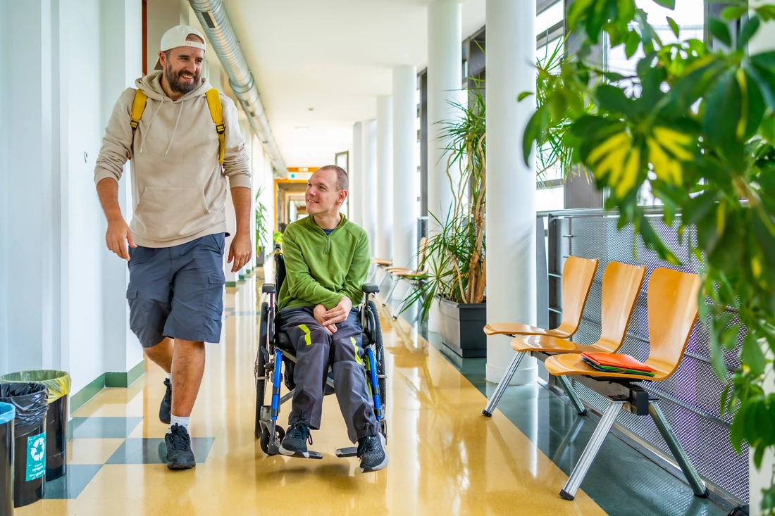 Man with physical disability in wheelchair and friend chatting distracted in the university