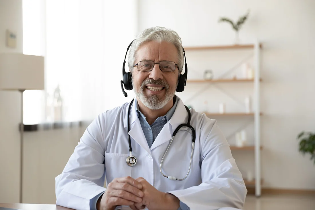Smiling senior old doctor wears headset looking at camera Remote online medical chat consultation, tele medicine distance services, virtual physician conference call, telemedicine concept Portrait