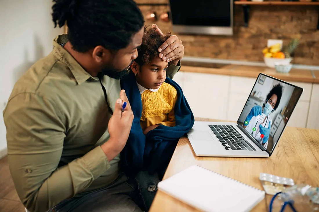 African American father and his sick daughter using laptop while having video call with family doctor during coronavirus pandemic Focus is on daughter