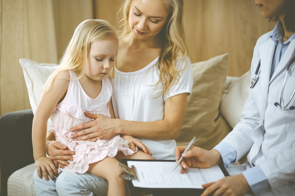Doctor and patient. Pediatrician using clipboard while examining little girl with her mother at home. Sick and unhappy child at medical exam. Medicine concept